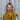 Hanna Somatics teacher, Karen, is standing against a wooden gate wearing a yellow garter stitch shawl in Lore