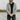 Ingemar is wearing a v-neck cardigan over a black t-shirt and jeans. He has his hands clasped in front of him and he's looking down. Lowther Cardigan Knitting Pattern