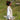 A woman wears a roll-neck handknit vest over a white shirt and stands in a sunlight grassy field